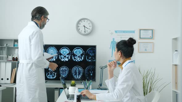 Doctors Male and Female Analyzing Brain Scans and Discussing Disease in Hospital Room