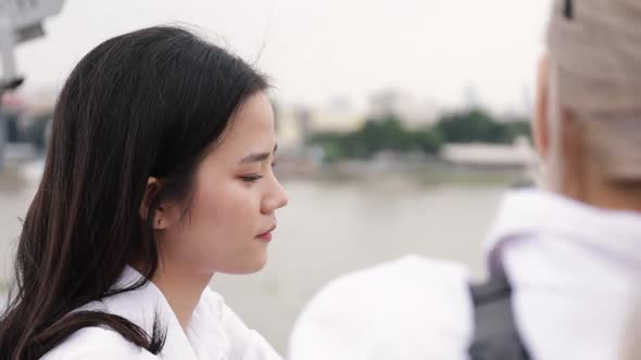 Asian lesbian couple talking while standing on the bridge.