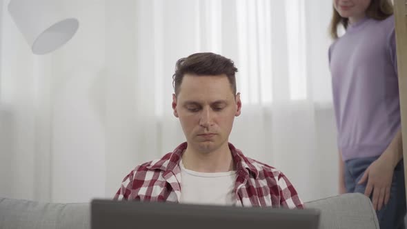 Young Woman Hugging Busy Caucasian Millennial Man Typing on Laptop Keyboard