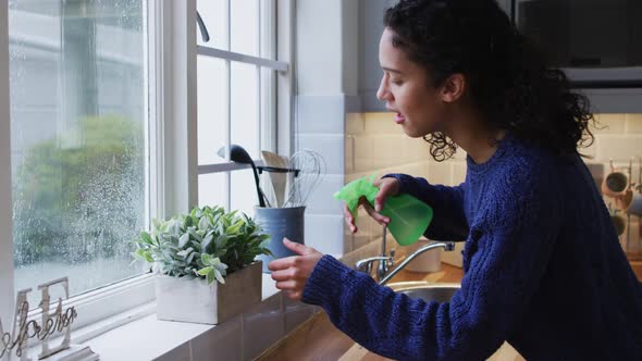 Mixed race woman watering plants in kitchen