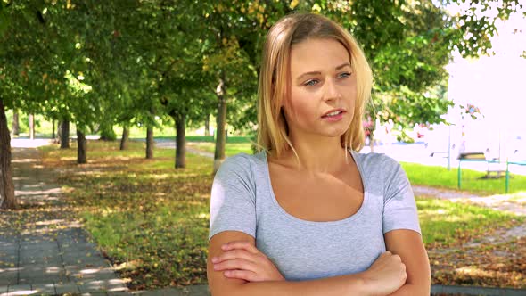 Young Pretty Blond Woman Walks and Thinks About Something - Park with Trees in Background