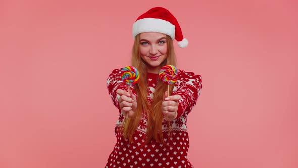 Joyful Girl in Red Christmas Sweater Hat Presenting Candy Striped Lollipops Stretches Out Hands