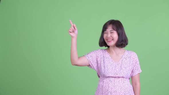 Happy Asian Pregnant Woman Thinking While Pointing Up