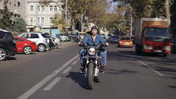 Two European Women Riding Motorcycle By the City Street Front View