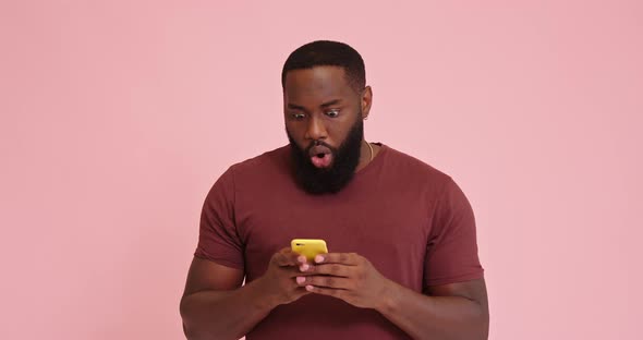 Young African American Man Using Phone Surprised Isolated on Pink Background