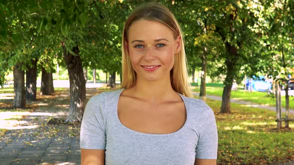 Young Pretty Blond Woman Invites - Park with Trees in Background