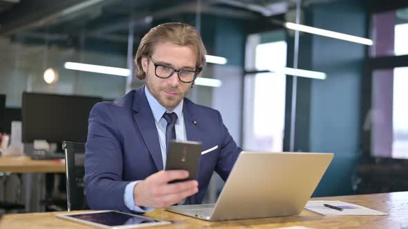 Businessman Using Smartphone and Laptop in Office