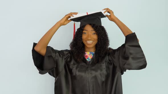 A Young African American Woman in a Black Gown and a Master's Hat Stands Upright Holding a Diploma