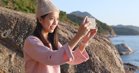 Woman taking photo on cellphone in seaside at sunset