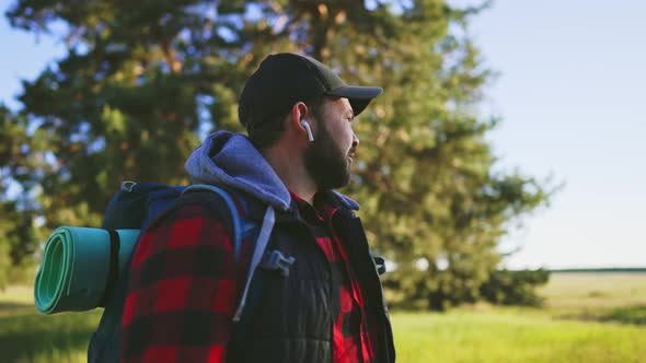 Man Traveler Walks Through Field with Backpack on His Shoulders