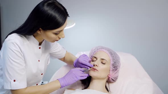 A cosmetologist in a white lab coat performs procedure of lip augmentation for a client