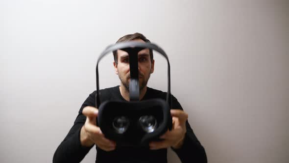 A man standing against a gray wall takes the VR glasses off his head and puts them on you