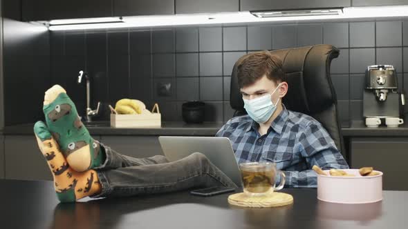 Man using protective medical face mask while working on laptop at home to prevent coronavirus 