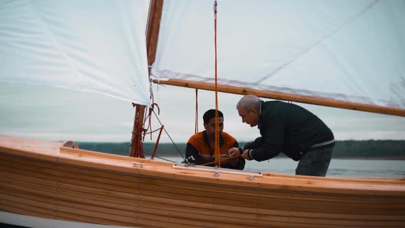 Wood Sailboat with Two Men Working with Sail.