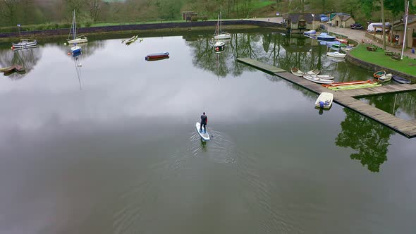 Beautiful aerial view, footage of middle aged man paddle boarding on Rudyard Lake in the Derbyshire