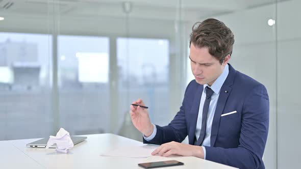 Disappointed Young Businessman Trying To Write on Paper 