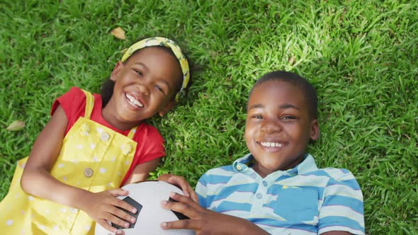 Animation of happy african american siblings lying on lawn and holding ball