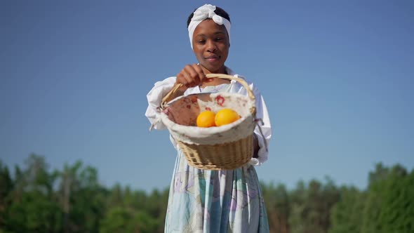 Portrait of Satisfied African American Woman Showing Basket with Organic Oranges Looking at Camera