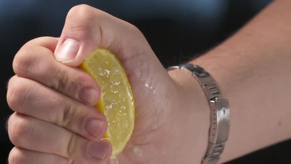 A fresh, juicy lemon is squeezed by a male hand wearing wristwatch. Shot in high speed photography.