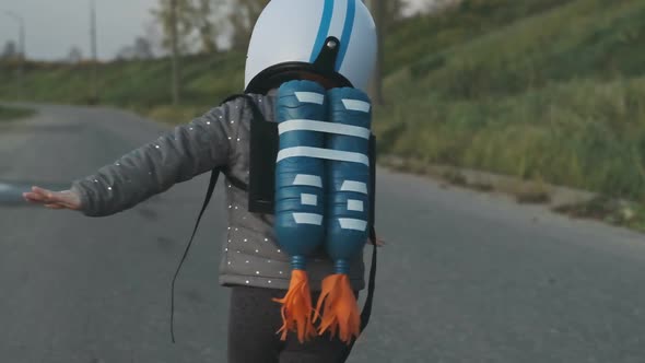 Cute Girl Running on Rural Road Wearing Helmet and Jetpack, Acting To Be Pilot