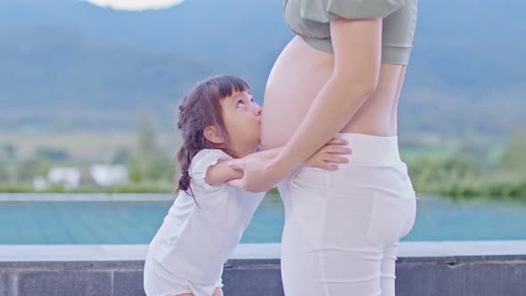 Adorable kid girl hugging and kissing pregnant mother belly