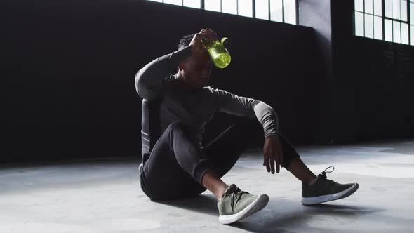 African american man sitting in an empty building pouring water on his head