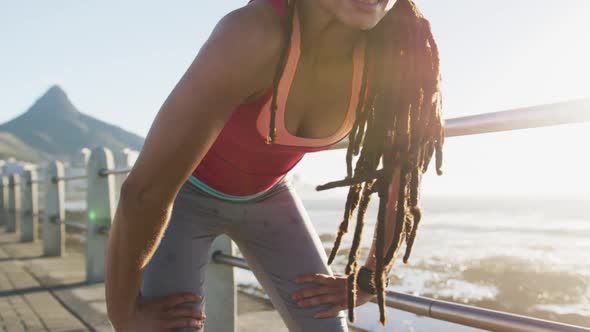 African american woman exercising resting on promenade by the sea