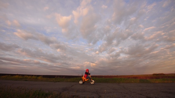 Little boy on a tricycle rides on a scenic rural road at sunset