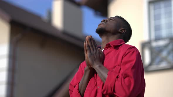 Religious African American Young Man with Clasped Hands Praying Standing in Sunlight Outdoors