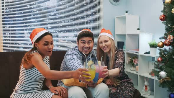 Three Smiling Friends in Santa Hats Making Cheers with Cocktails