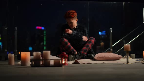 Wide Shot Tired Caucasian Woman Sitting in Darkness on Roof in Urban City with Candles Burning