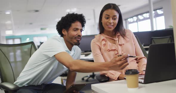 Video of happy diverse businesswoman and businessman using laptop and talking