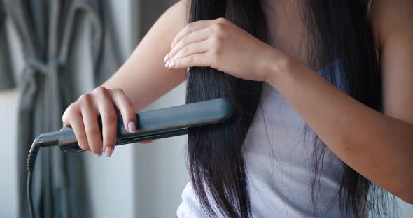 Closeup of Unrecognizable Woman with Beautiful Bright Healthy Long Hair Using Flat Iron Straightener