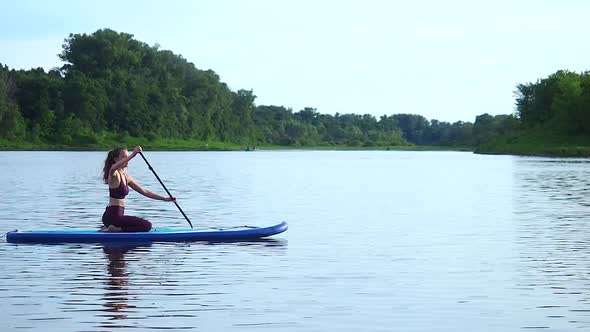 Woman Pushing and Pulling the Paddle Through Shining Water Surface and Propelling Paddleboard on