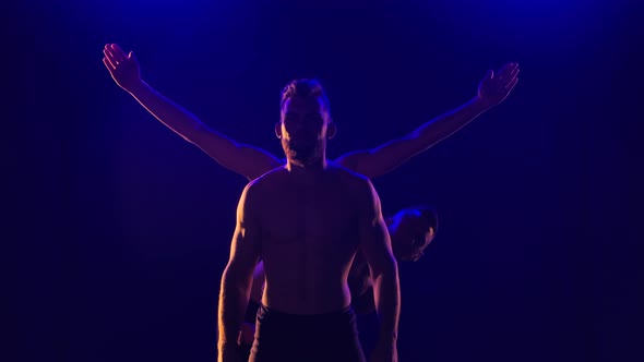 Group of Acrobatic Gymnasts Perform Acrobatic Exercises. Shot in a Dark Studio with Blue Light. Slow