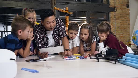 Group of Six Caucasian School Children Watching their Asian Male Teacher