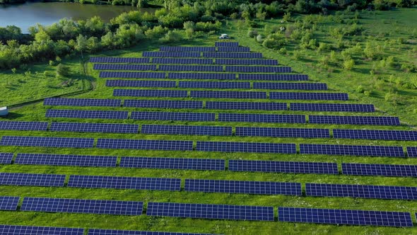 Aerial view on Solar Power Station in Green Field near River at Sunny Day. Fly over Solar Farm