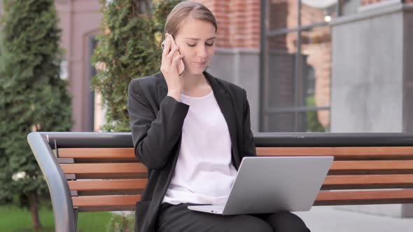 Young Businesswoman Talking on Phone, Sitting on Bench