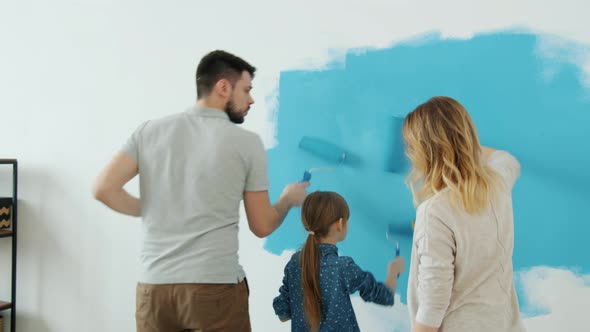 Back View of Adorable Young Family Mum Dad and Daughter Painting Wall in Apartment