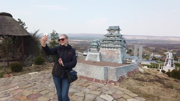 Girl Takes a Selfie Near a Miniature Chinese Japanese Pagoda. Park of Miniatures.