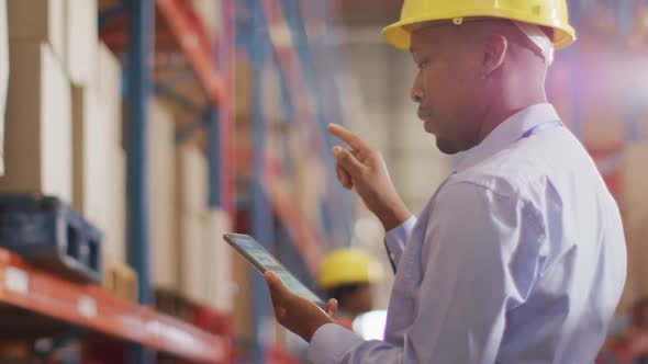 African american male worker with helmet using smartphone in warehouse