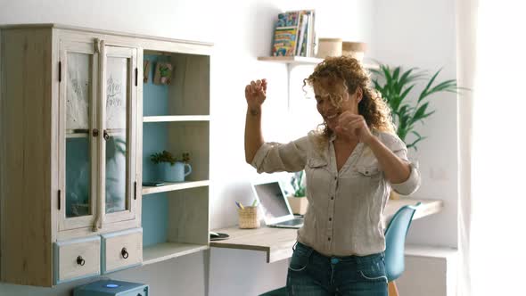 Excited and joyful middle age woman dancing at home singing a song for happiness