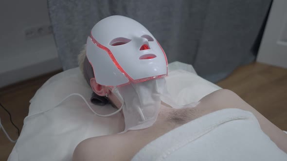 Young Caucasian Man Lying on Beauty Bed with Red LED Light Device on Face
