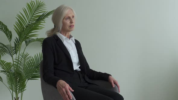 Elderly Woman in a Business Suit is Sitting in a Chair Looking Out the Window