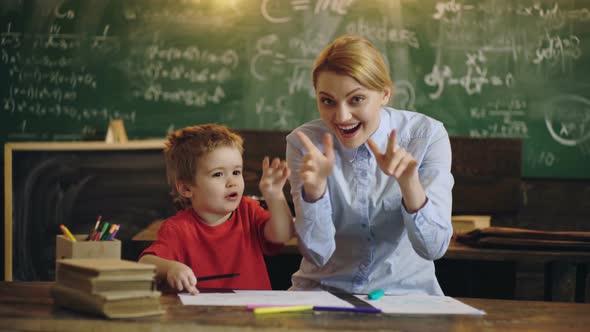 Pretty Teacher and Preschool Kid Smiling at Camera at Back of Classroom at the Elementary School.