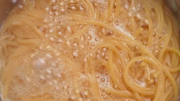 Raw spaghetti is being cooked in boiling water in a kitchen pot.