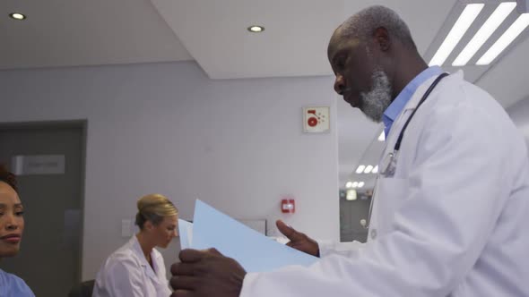 Diverse male doctor at hospital reception and talking to female staff