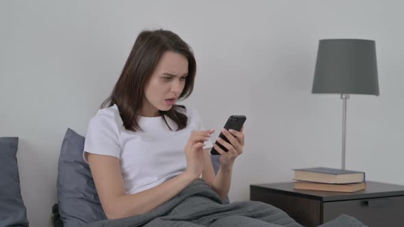Woman Reacting to Loss on Smartphone in Bed