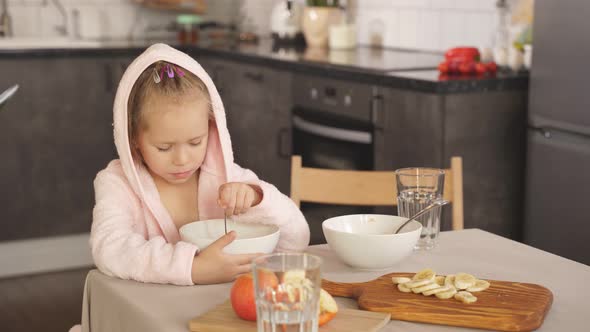 Little Girl Sits at the Table and Has Breakfast Oatmeal Porridge with a Banana