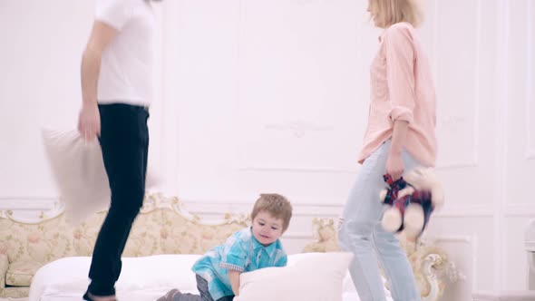 Happy Family Jumping on the Bed and Throwing Pillows. Father, Mother and Son Jump with Cushions on